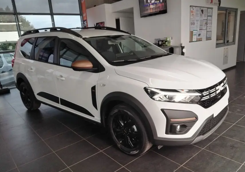 Vue 3/4 avant d'un Dacia Jogger blanc avec rétroviseurs cuivrés et jantes noires en showroom.