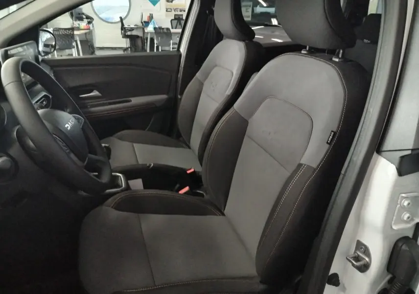 Vue intérieure côté conducteur du Dacia Jogger blanc 2025, sièges bi-matière gris et noir avec surpiqûres contrastantes.