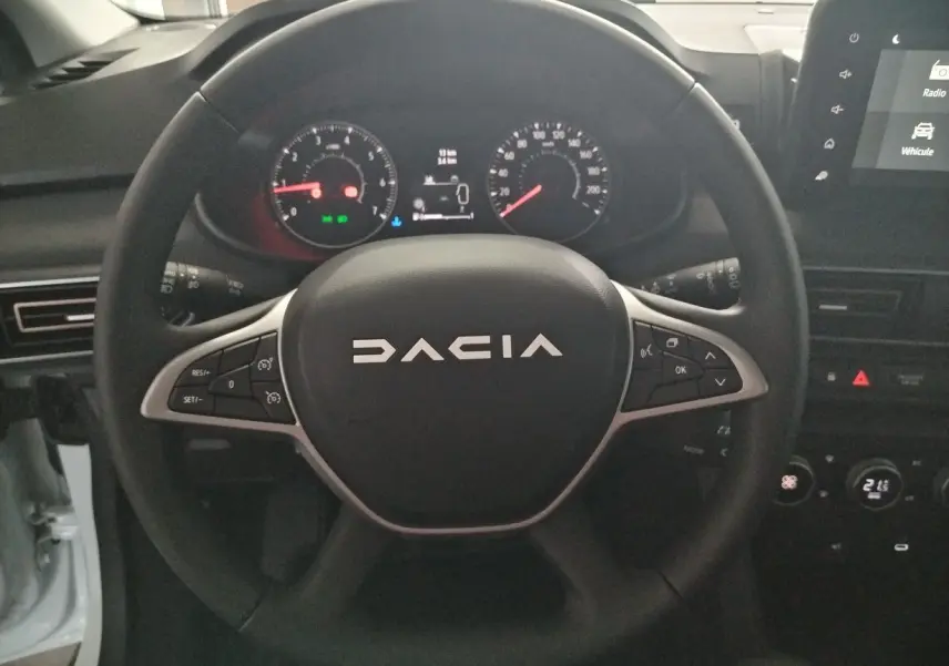 Vue rapprochée du volant noir DACIA avec commandes intégrées et tableau de bord numérique du Jogger blanc 2025.