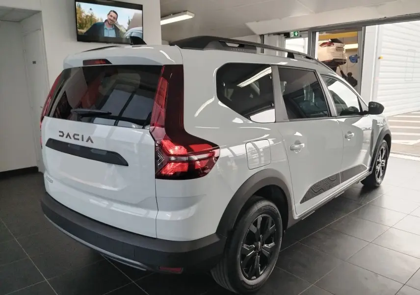 Vue 3/4 arrière droite du Dacia Jogger blanc avec barres de toit modulables et jantes noires en showroom.