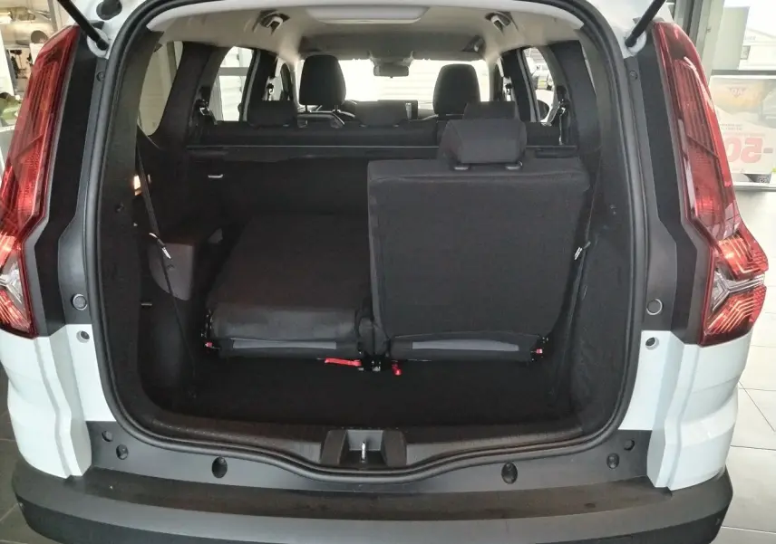 Vue arrière du coffre ouvert d'un Dacia Jogger blanc 2025, montrant les sièges arrière partiellement rabattus.