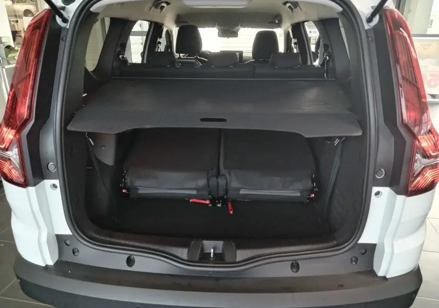 Vue arrière ouverte du coffre du Dacia Jogger blanc 2025, montrant la tablette cache-bagages et les sièges rabattus.