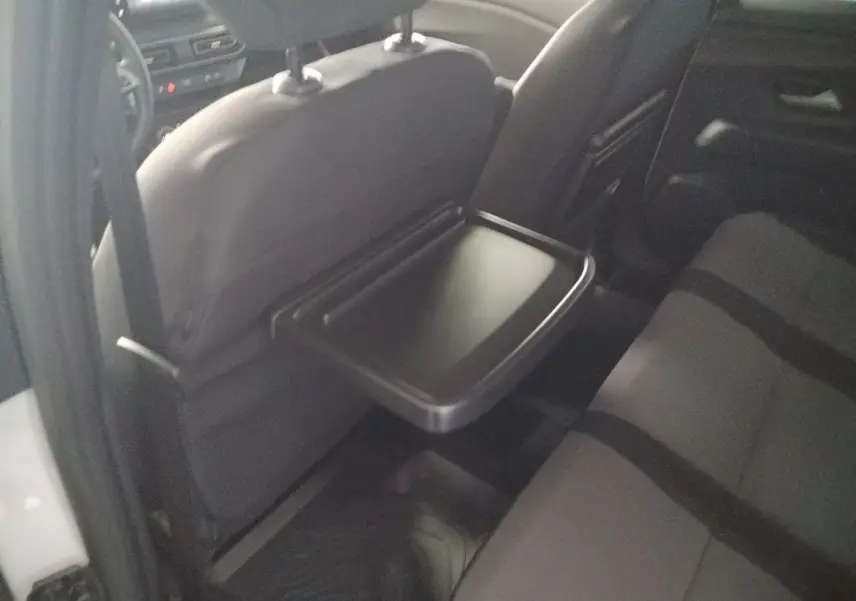 Vue intérieure arrière droite du Dacia Jogger blanc 2025, mettant en valeur la tablette rabattable sur le siège avant.