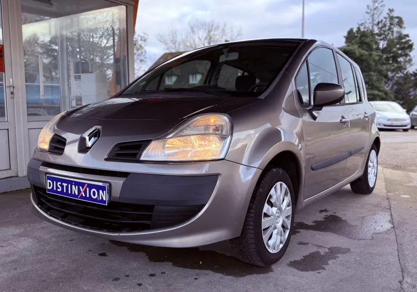 Renault Modus beige vue 3/4 avant droit avec phares allumés et plaque Distinxion visible.