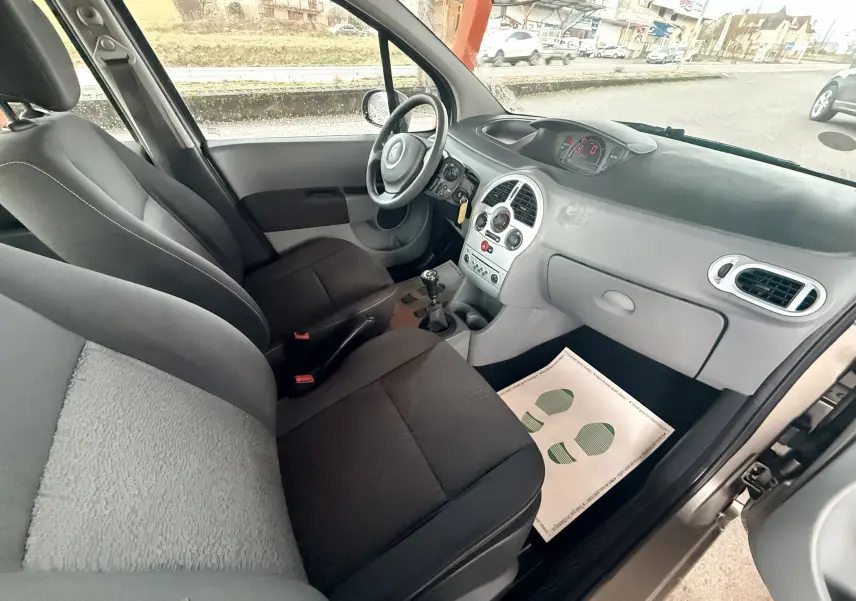 Vue intérieure côté conducteur du Renault Modus beige 2011, montrant les sièges tissu gris et noir et le tableau de bord gris clair.