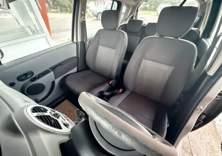 Vue intérieure côté conducteur de la Renault Modus beige, montrant les sièges avant gris et le volant en cuir.