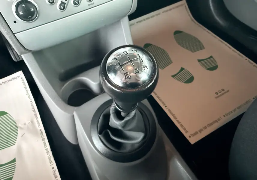 Gros plan sur le levier de vitesses manuel de la Renault Modus beige, avec console centrale et tapis de sol visibles.