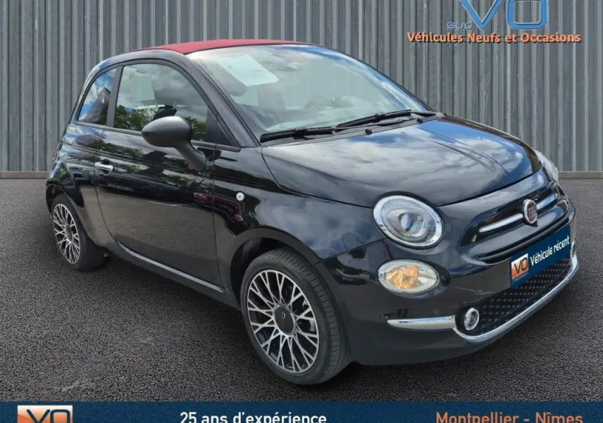 Vue 3/4 avant droite d'une FIAT 500C noire 2024 avec toit rouge, jantes alliage et roue de secours visible.