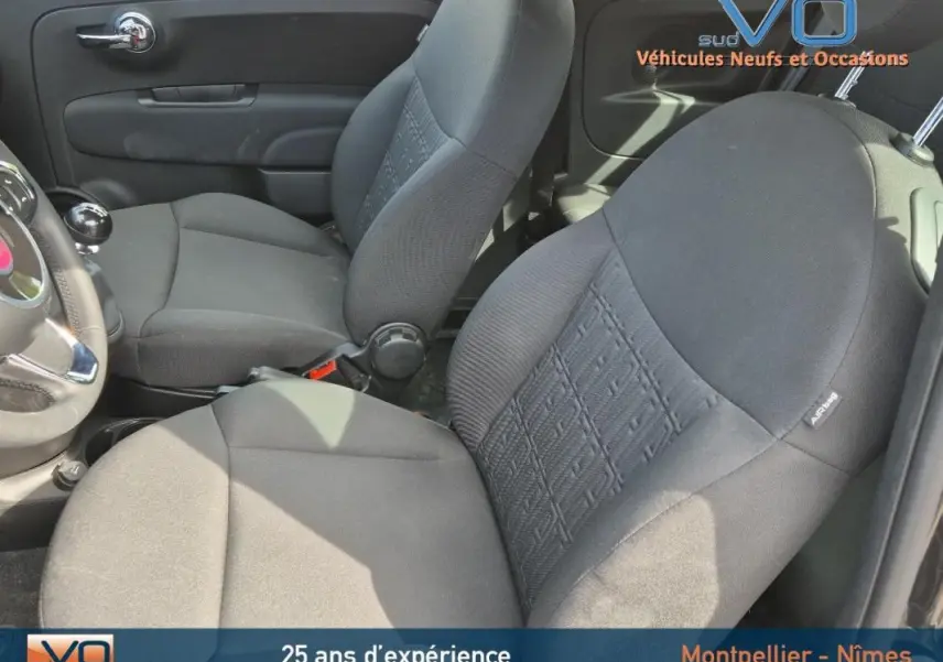 Vue intérieure côté gauche montrant les sièges avant noirs du Fiat 500C 2024 avec volant et levier de vitesses manuelle.