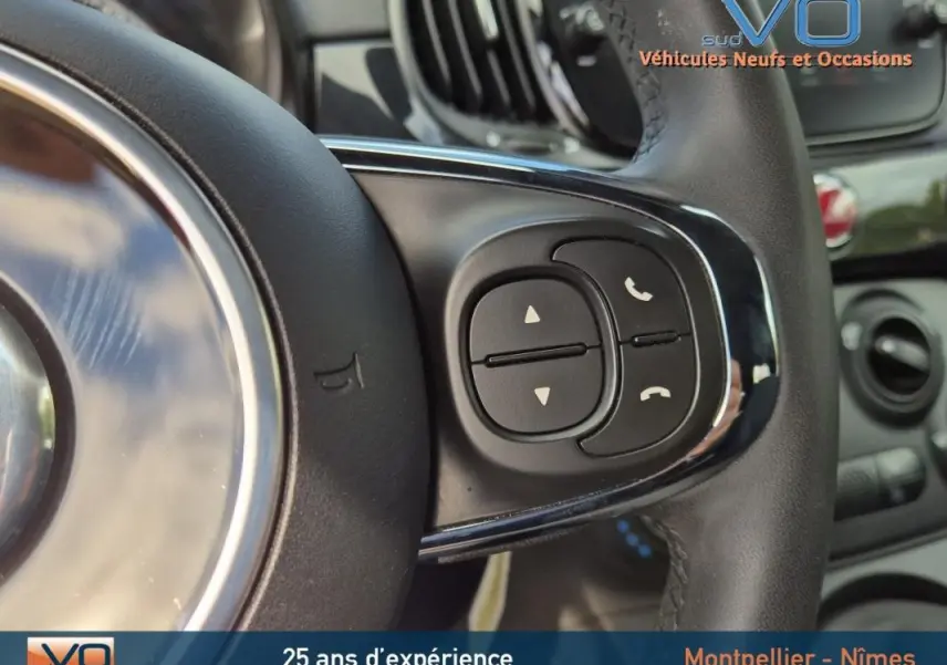 Gros plan sur les commandes au volant côté droit de la FIAT 500C noire 2024 avec volant en cuir et finition brillante.