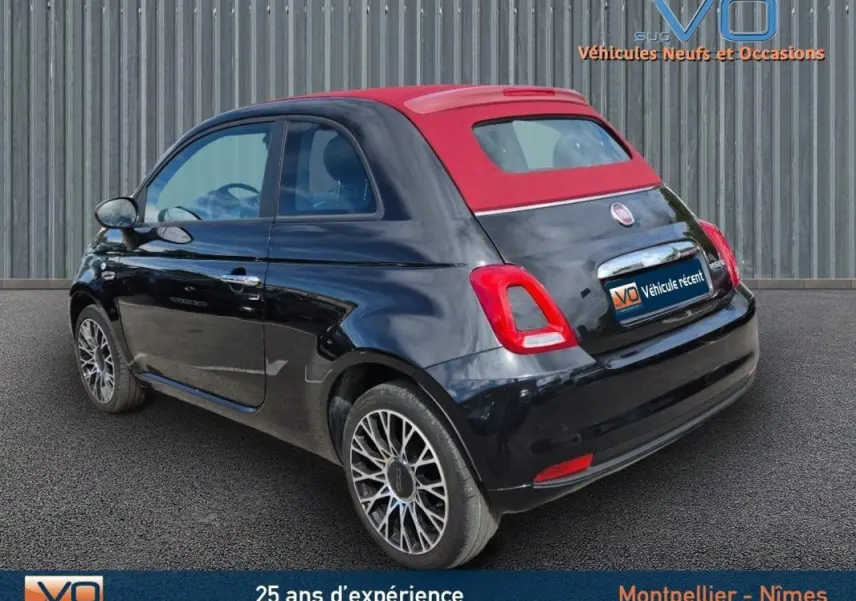 Vue 3/4 arrière droite d'une Fiat 500C noire 2024 avec toit rouge et roue de secours visible sur jante stylée.