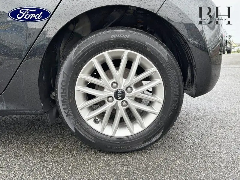 Gros plan sur la roue avant droite d'une KIA RIO noire Ébène avec jante alliage et logo central Kia visible.