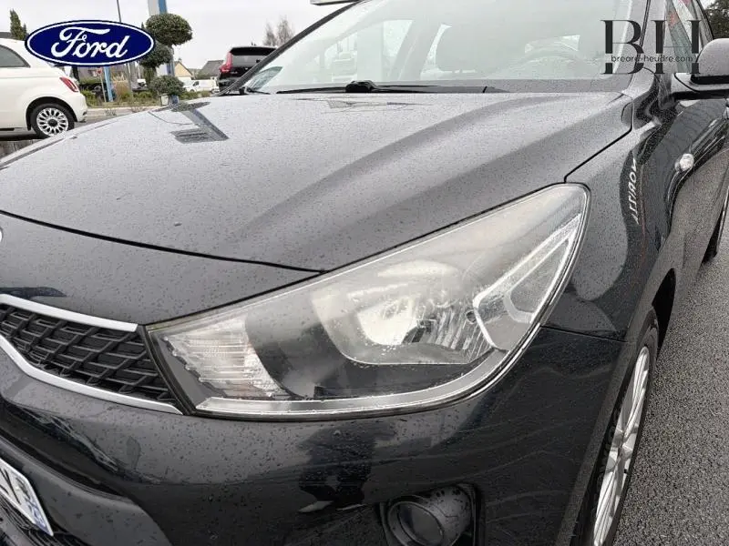 Vue 3/4 avant droit d'une KIA Rio noire Ébène 2018, mettant en valeur le phare et la calandre chromée.