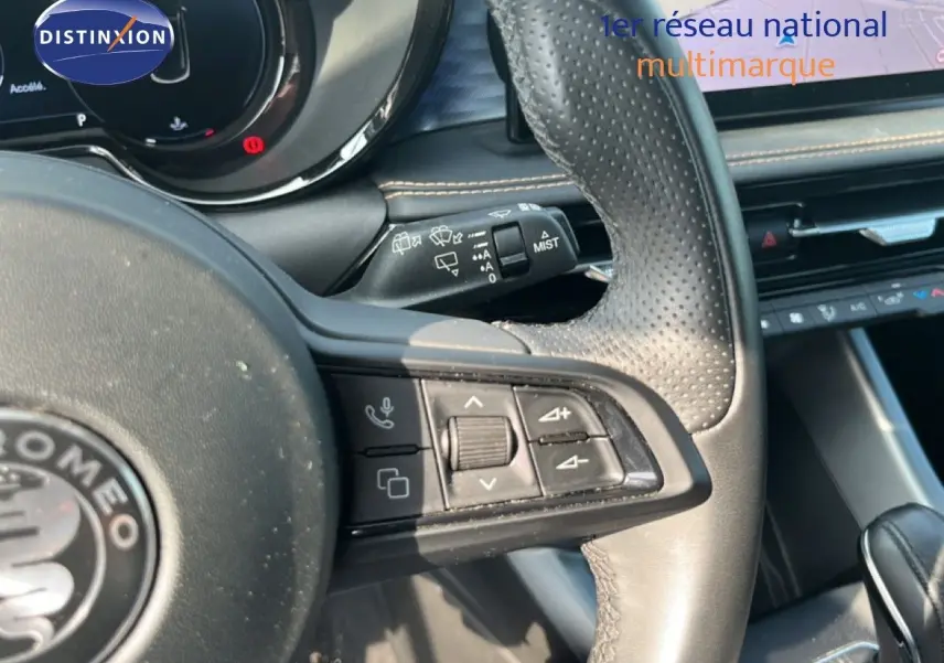 Gros plan sur le volant en cuir perforé noir de l'Alfa Romeo Tonale 2023, avec commandes intégrées et tableau de bord partiel.