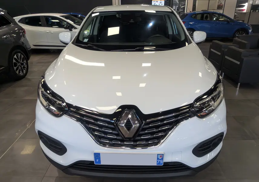 Vue de face d'un Renault Kadjar blanc Glacier 2021 en showroom, avec calandre noire et logo Renault proéminent.