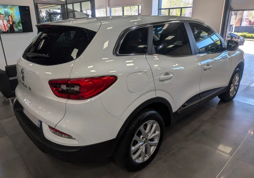 Vue 3/4 arrière droite d'un Renault Kadjar blanc Glacier 2021 en showroom, avec feux arrière rouges et jantes argentées.