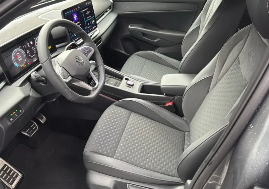 Vue intérieure côté conducteur du Volkswagen T-Roc 2026, sièges tissu gris, volant cuir multifonctions et tableau de bord digital.