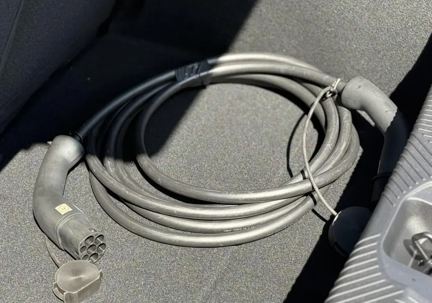 Câble de recharge électrique noir enroulé dans le coffre d'une Renault R5 E-Tech blanc nacré, vue rapprochée.