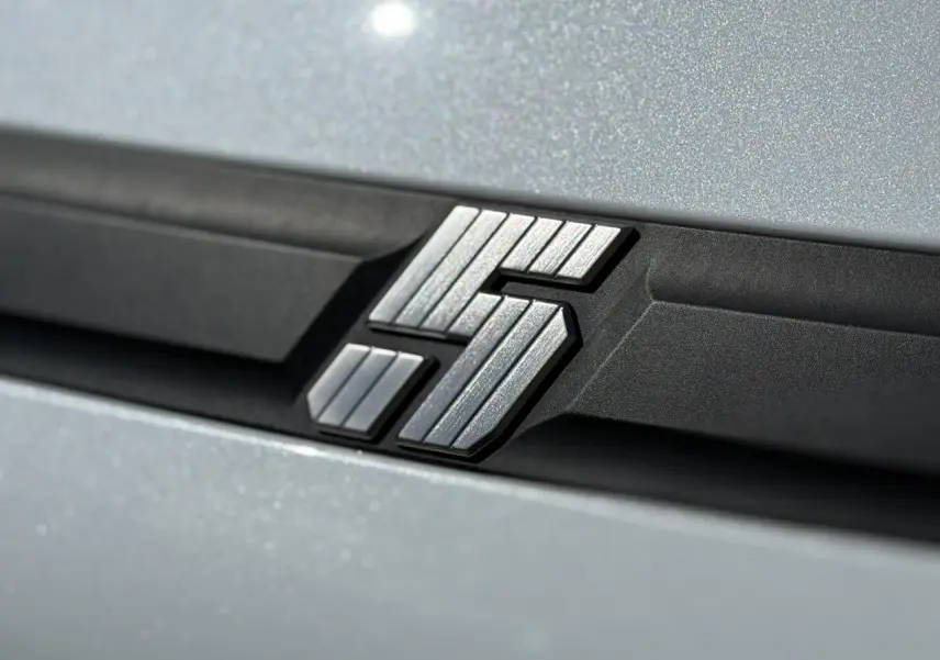 Gros plan sur le logo E-Tech argenté sur fond noir, sur la carrosserie blanc nacré de la Renault R5 électrique.