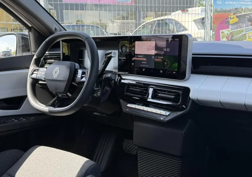 Vue intérieure côté conducteur de la Renault R5 E-Tech 2026, tableau de bord blanc nacré avec écran tactile central et volant multifonction.