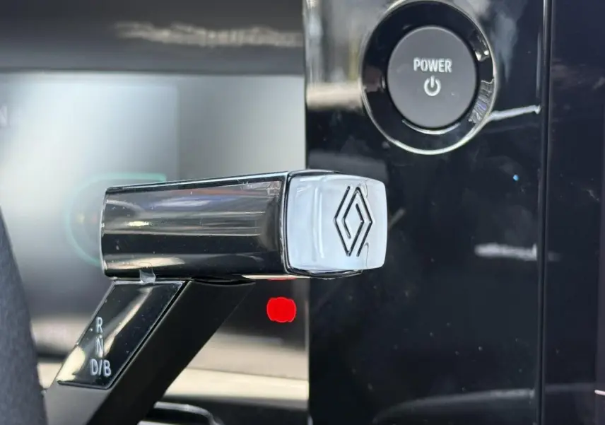 Gros plan sur le levier de vitesses noir brillant avec logo Renault, bouton Power en arrière-plan noir.