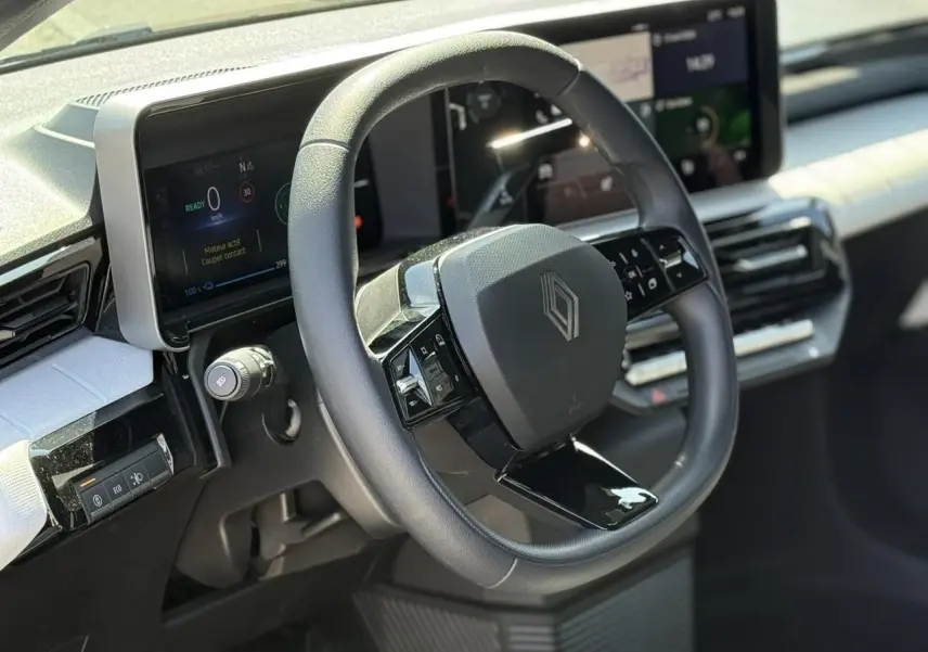 Vue intérieure centrée sur le volant multifonction noir et le tableau de bord numérique de la Renault R5 E-Tech blanc nacré.