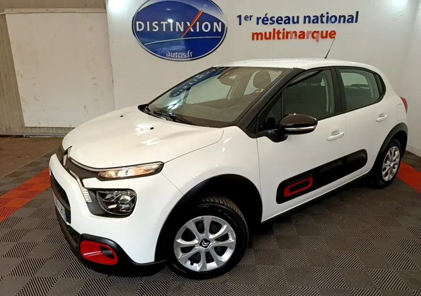 Citroën C3 blanche vue 3/4 avant droit, avec inserts rouges distinctifs sur les protections latérales et pare-chocs.
