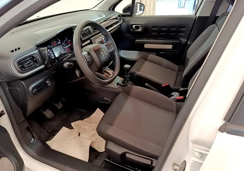 Vue intérieure côté conducteur d'une Citroën C3 blanche de 2021, montrant le tableau de bord et les sièges noirs.