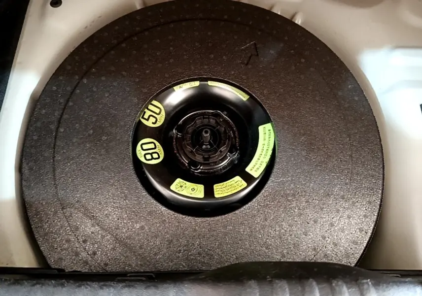 Vue en plongée sur la roue de secours compacte noire dans le coffre d'une Citroën C3 blanche.
