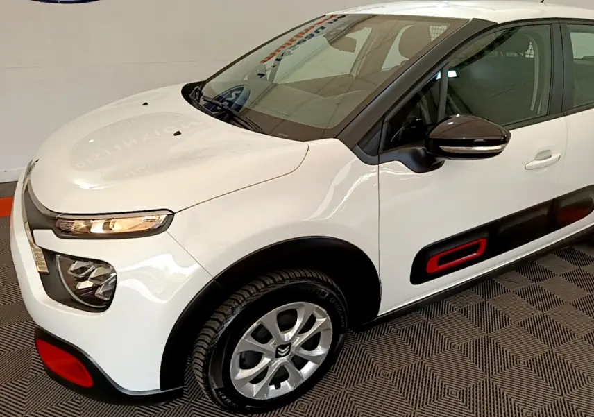 Vue 3/4 avant droite d'une Citroën C3 blanche avec inserts rouges sur les protections latérales et pare-chocs.
