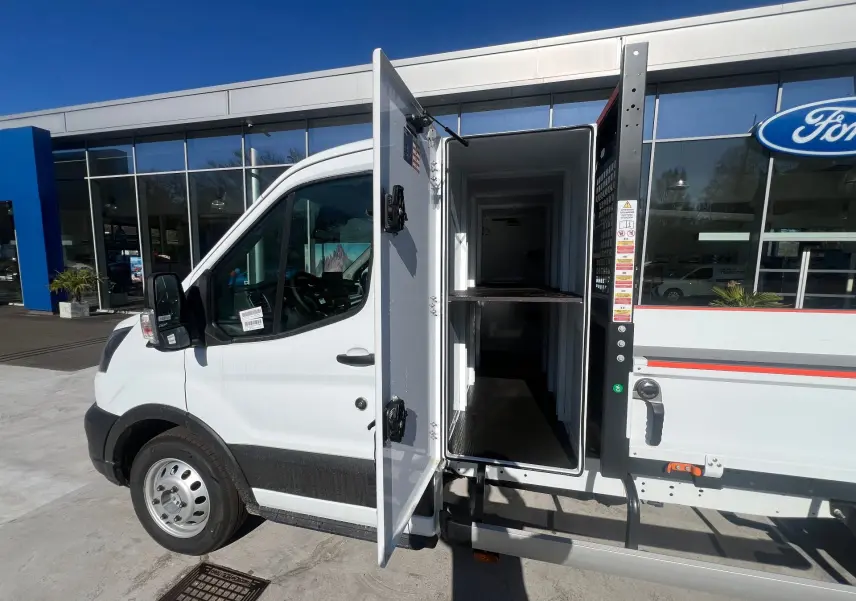 Vue de côté gauche d’un Ford Transit Chassis Cabine blanc avec porte latérale ouverte montrant la benne et le coffre intégré.