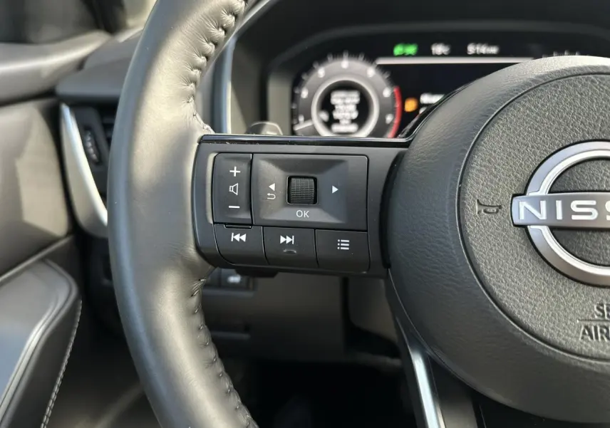 Gros plan sur le volant cuir noir du Nissan Qashqai 2025, avec commandes multifonctions côté gauche et tableau de bord numérique en arrière-plan.