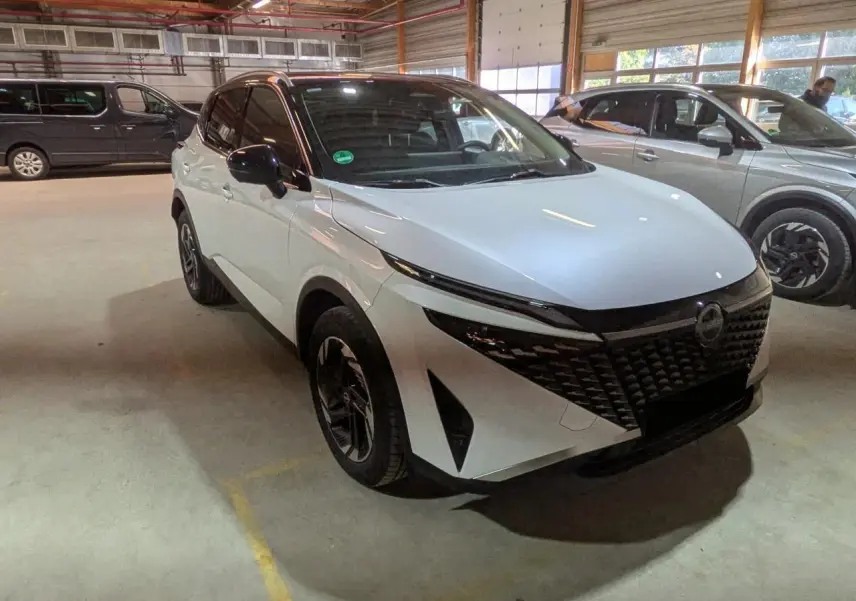 Nissan Qashqai blanc nacré et noir en 3/4 avant droit, avec calandre noire et jantes alliage 18 pouces.