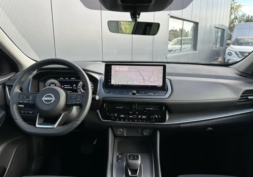 Vue intérieure avant du Nissan Qashqai 2025 avec tableau de bord noir, écran tactile central et volant cuir multifonction.