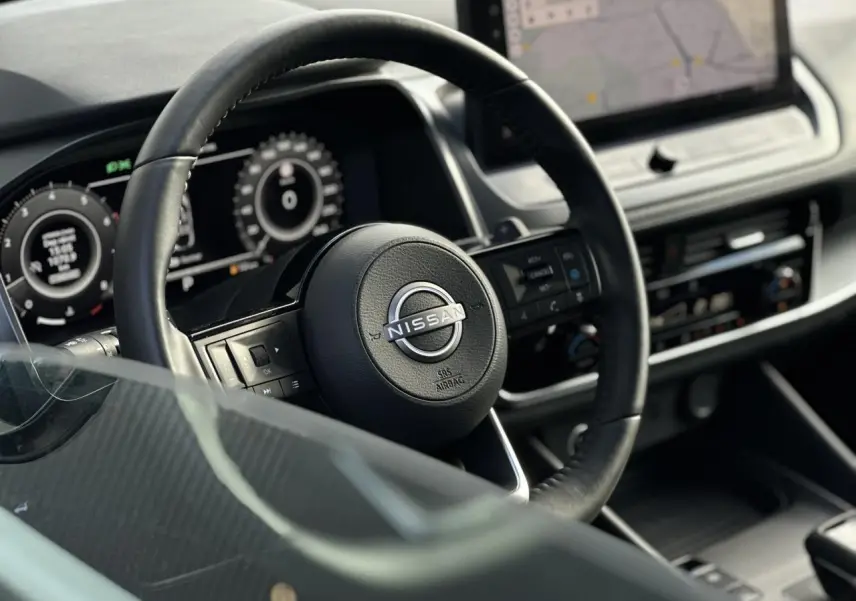 Vue rapprochée du volant cuir noir Nissan Qashqai 2025 avec tableau de bord numérique et écran tactile central.