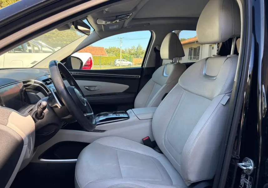 Vue intérieure côté conducteur du Hyundai Tucson noir 2022, sièges cuir gris clair et volant cuir avec console centrale.