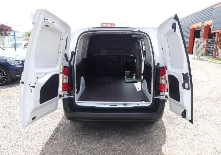Vue arrière d'un Peugeot Partner blanc 2025 avec portes arrière ouvertes et plancher bois antidérapant visible dans la zone de chargement.