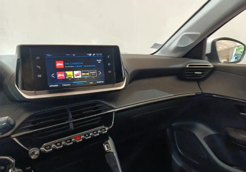 Vue intérieure côté passager du tableau de bord noir et écran tactile 7 pouces de la Peugeot 208 blanche PureTech 2020.