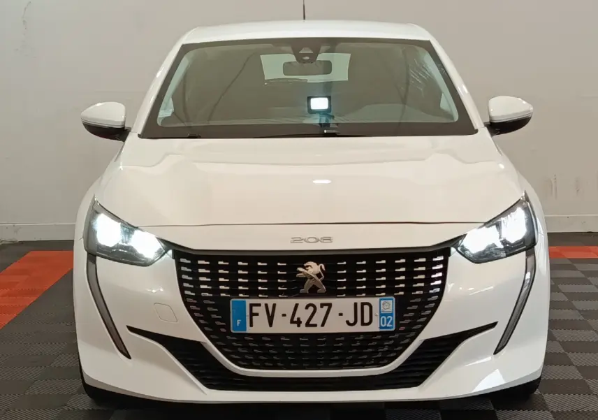 Vue frontale d'une Peugeot 208 blanche de 2020 avec phares LED allumés et calandre noire distinctive.