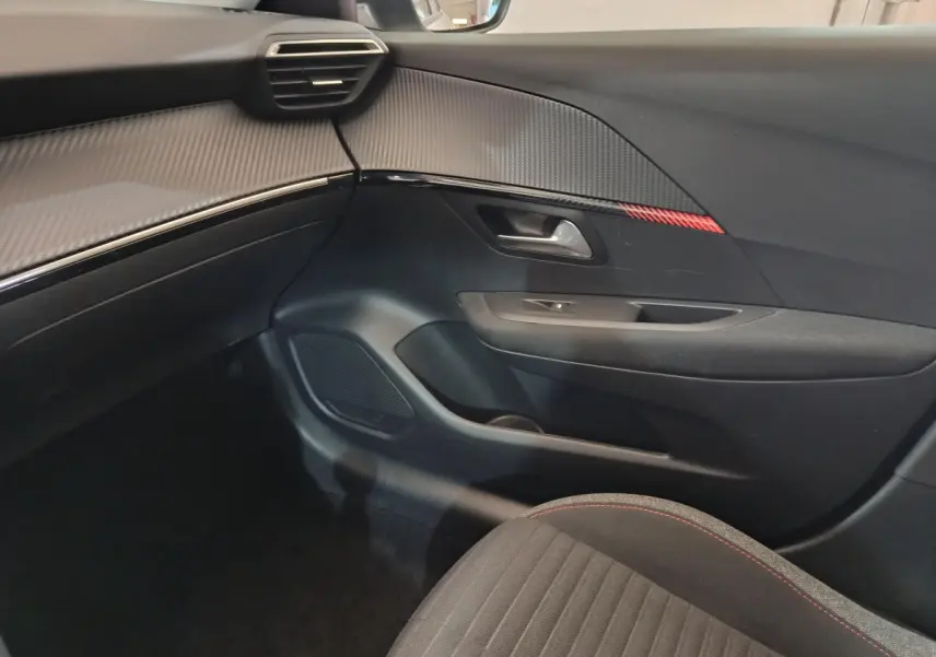 Intérieur côté passager du Peugeot 208 blanc, avec garniture noire et surpiqûres rouges sur le siège.