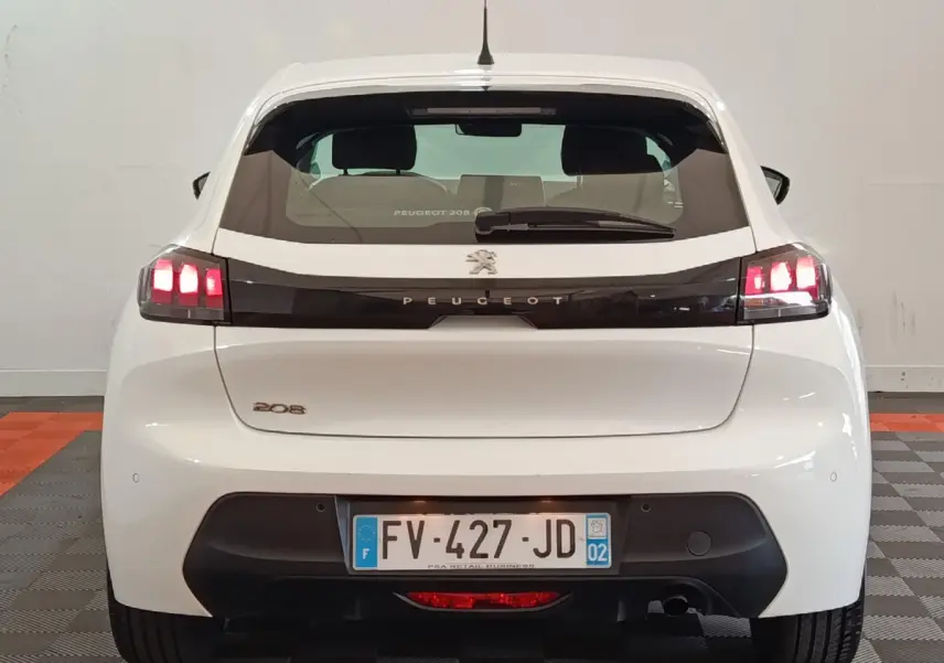 Vue arrière d'une Peugeot 208 blanche de 2020 avec feux LED allumés et logo Peugeot central sur hayon noir.