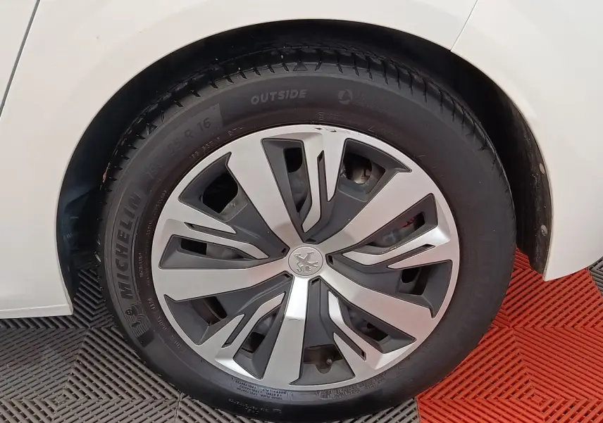 Gros plan sur la roue avant gauche blanche d'une Peugeot 208 PureTech 100 S&S Active Business avec jante en alliage moderne.