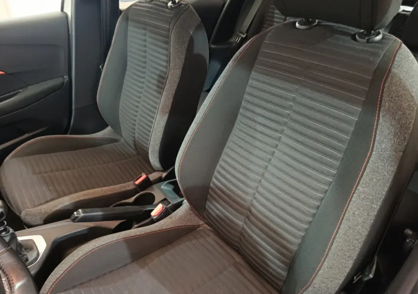 Vue rapprochée des sièges avant gris foncé avec surpiqûres rouges dans l'habitacle d'une Peugeot 208 blanche.