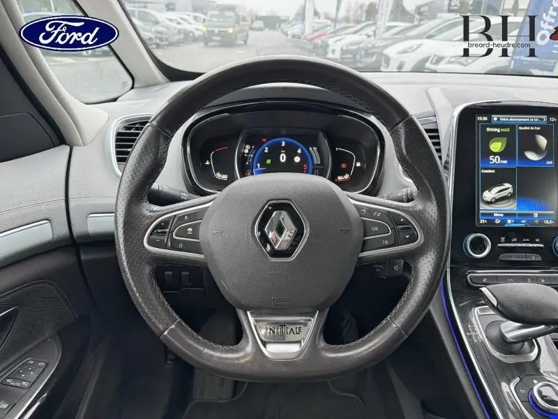 Vue intérieure centrée sur le volant cuir noir avec logo Renault et inscription Initiale, tableau de bord digital et écran tactile.