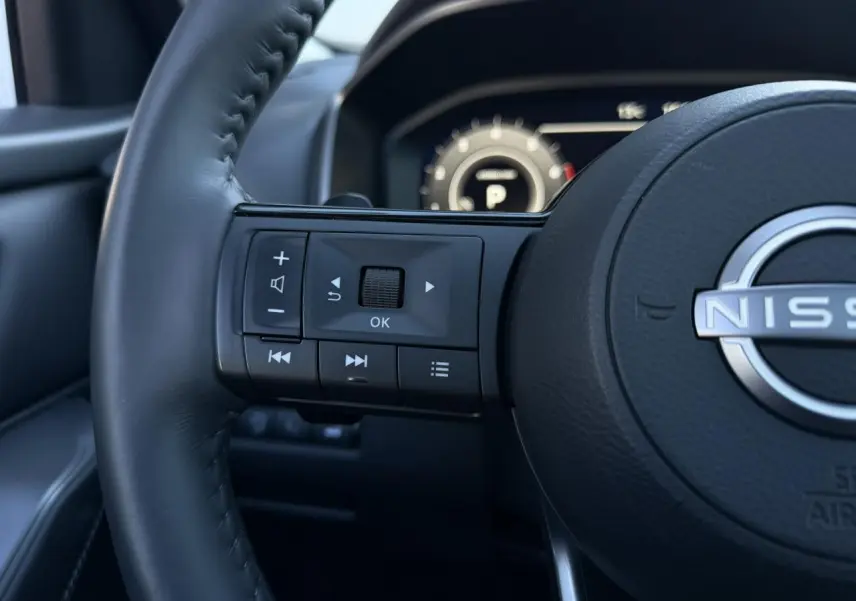 Gros plan sur le volant cuir noir du Nissan Qashqai 2025 avec commandes multifonctions et tableau de bord numérique flou.