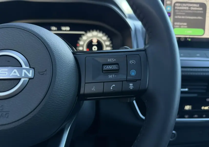 Gros plan sur le volant noir cuir du Nissan Qashqai 2025, avec commandes intégrées et tableau de bord numérique flou en arrière-plan.