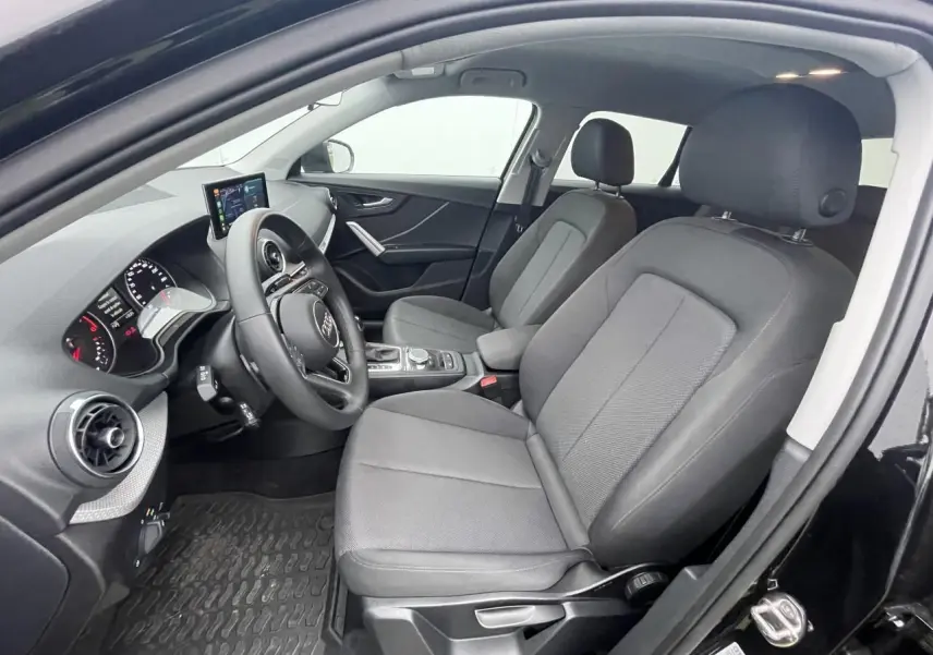 Vue intérieure côté conducteur de l'Audi Q2 noir mythic 2023, sièges tissu gris et tableau de bord moderne.