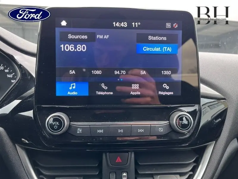 Écran tactile central de la Ford Fiesta 2022 affichant la radio FM avec commandes audio et design noir brillant.