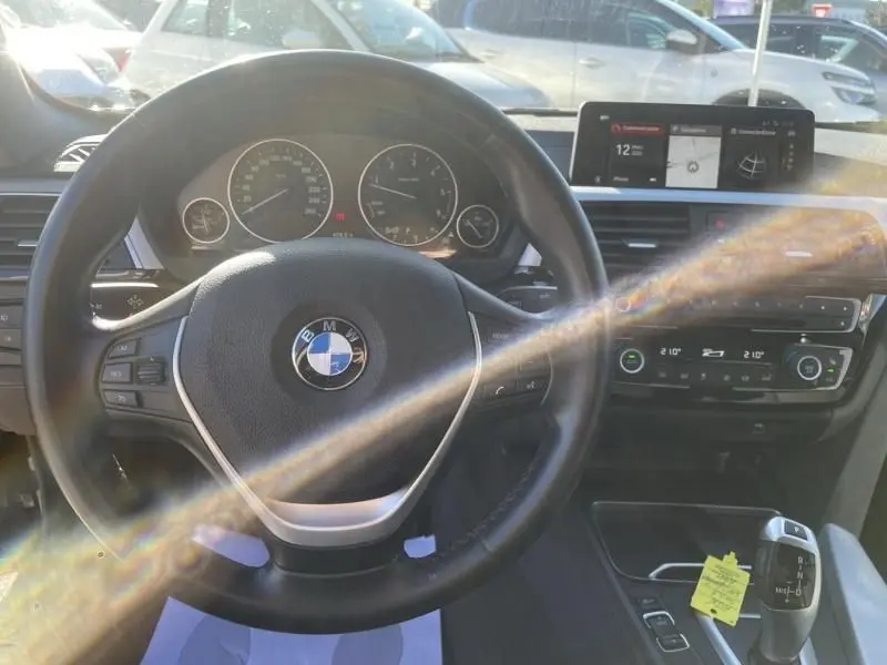 Vue intérieure centrée sur le volant BMW et le tableau de bord avec écran multimédia, ambiance lumineuse naturelle.