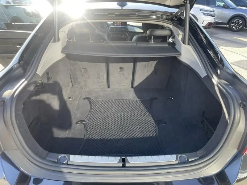 Coffre ouvert vu de l'arrière d'une BMW Série 4 Gran Coupé noir métal, montrant un espace de rangement propre avec filet.